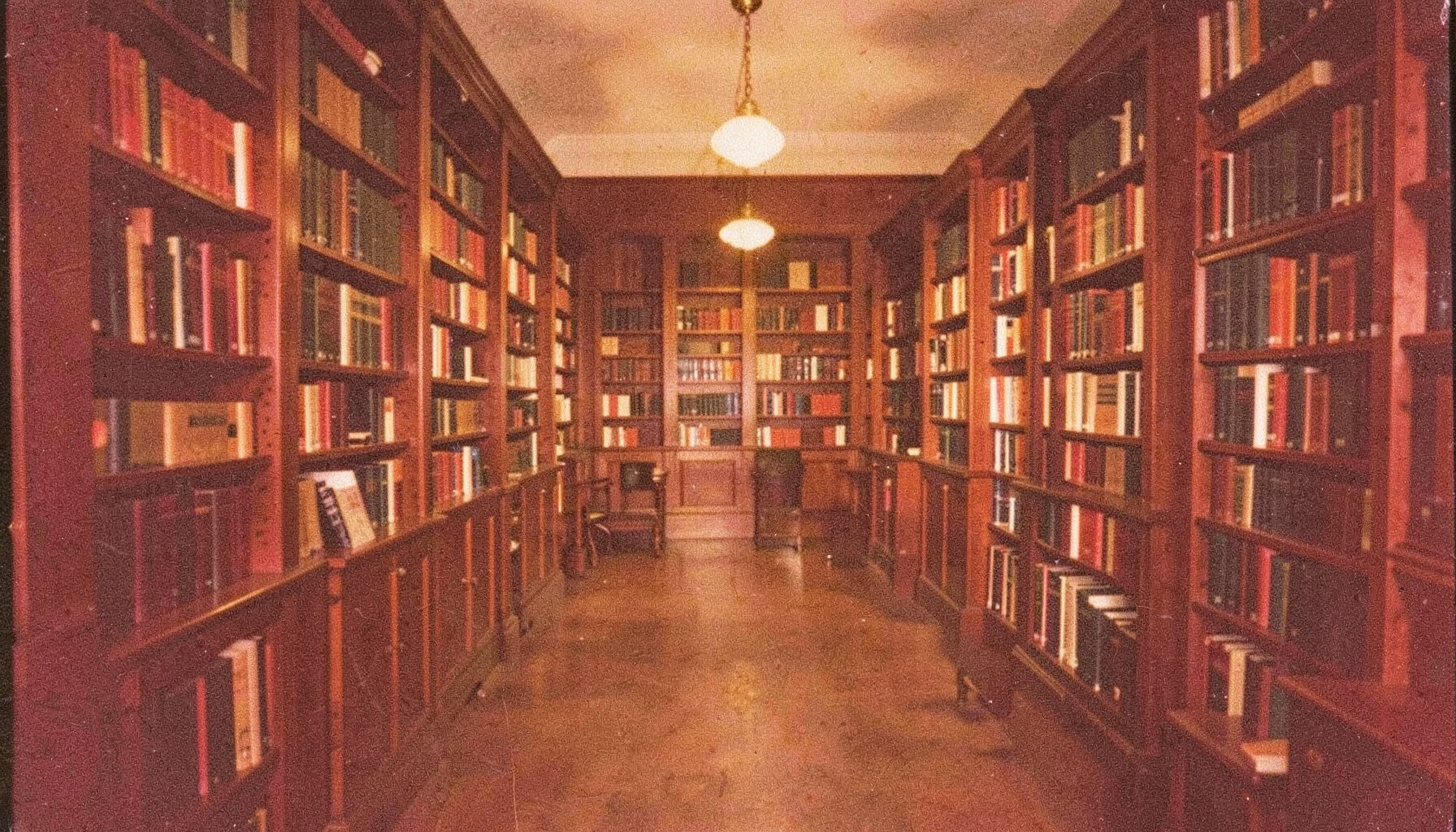 A grainy analog photograph of a quiet academic library interior with rows of bookshelves, warm amber lighting, and deep brown wood tones